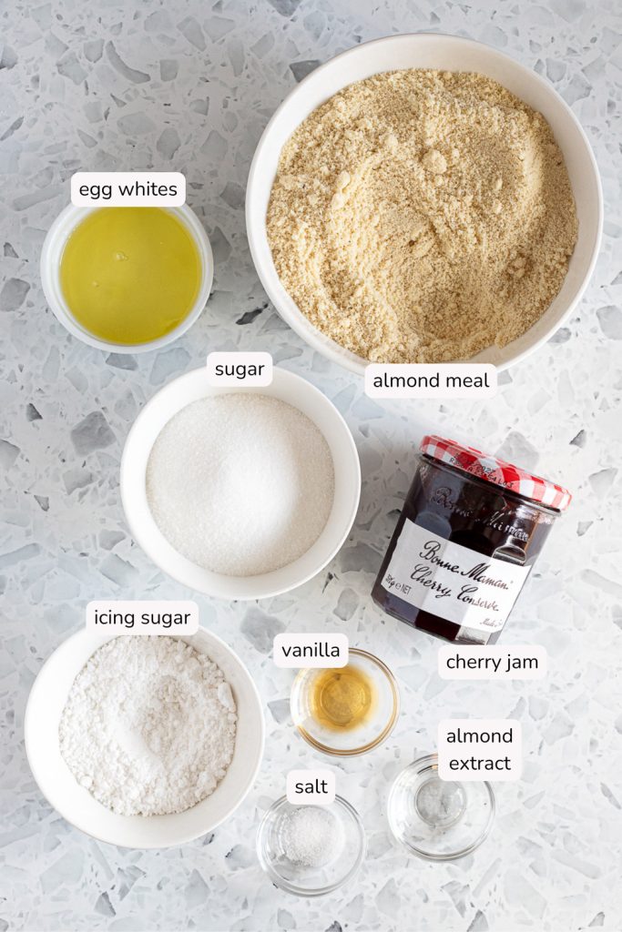 Overhead photo of labelled ingredients for cherry amaretti jam drops, including cherry jam, almond meal and egg whites.