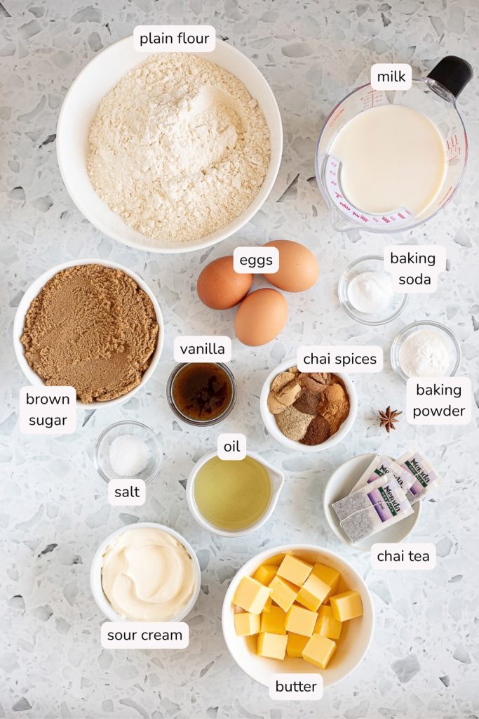 Overhead flat lay of labelled ingredients for vanilla chai cake layers, including chai tea bags, chai spices and brown sugar.