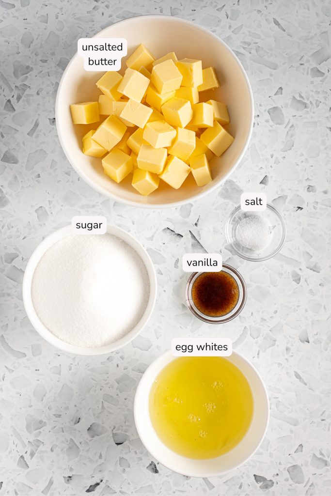 Labelled overhead photo of ingredients for vanilla Swiss meringue buttercream, including butter, egg whites, sugar and vanilla.