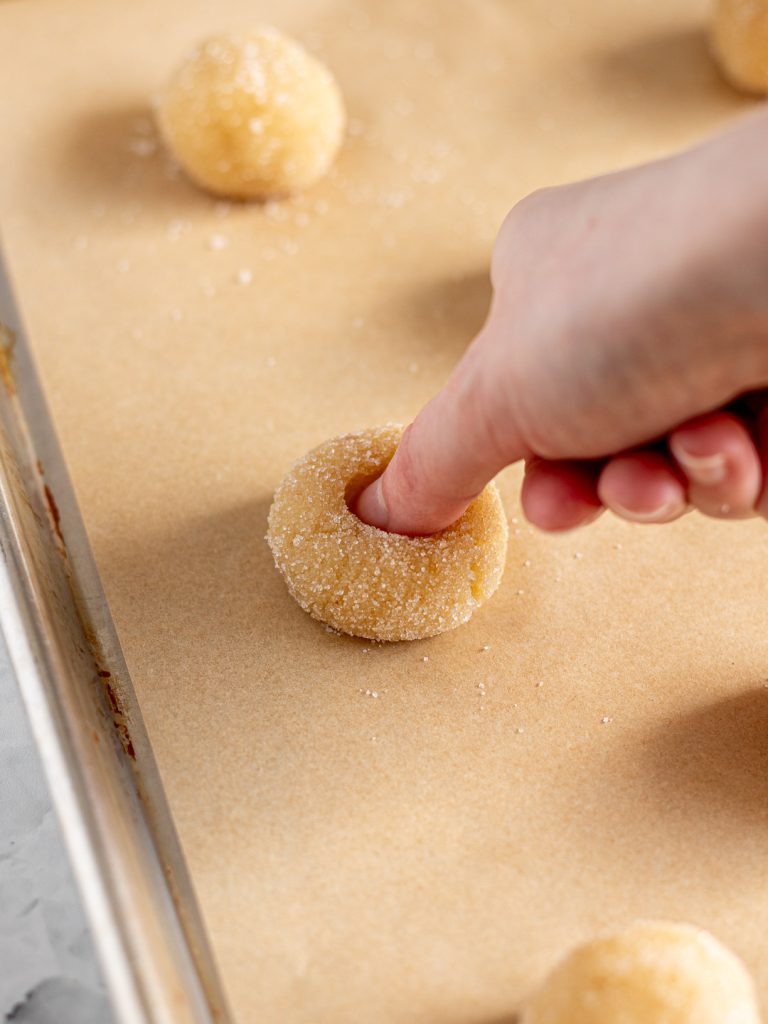 Thumb pressing an indent into the centre of each sugared amaretti dough ball.