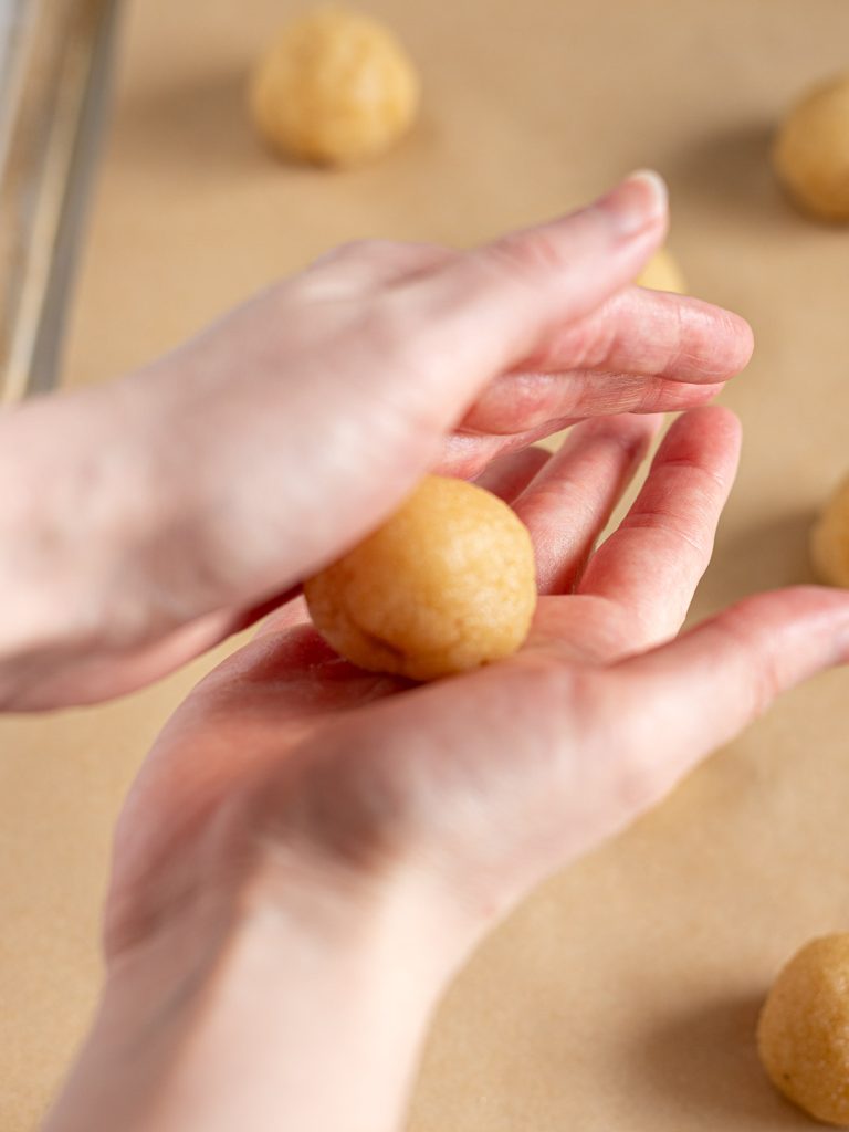 Hands rolling amaretti dough between the palms to form a smooth ball.