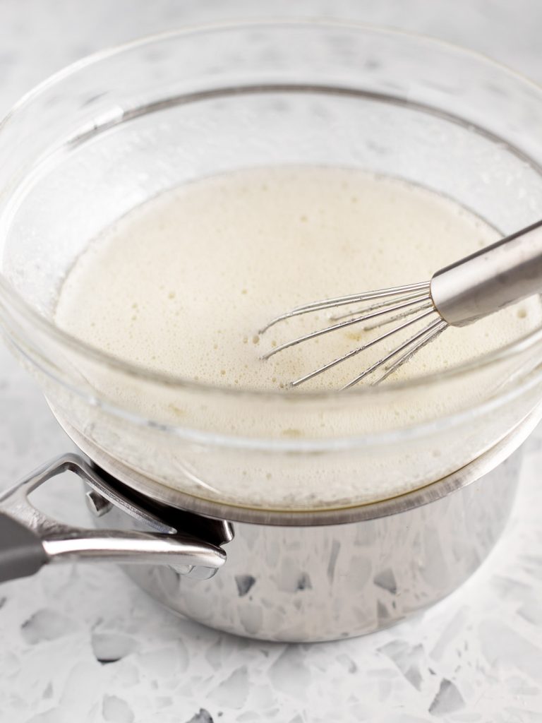 Egg whites and sugar whisked together in a bowl over a bain-marie, ready to be heated on the stovetop.