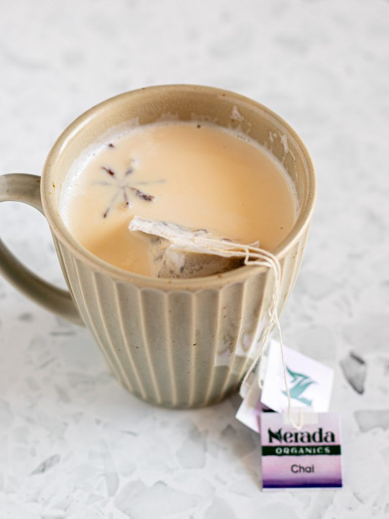 Chai tea bags steeping in star anise-infused milk in a muted green-grey mug.